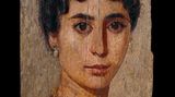 Eine Dame im Dreiviertelprofil mit dunklen Haar, glänzenden Ohrringen und einer Halskette mit Gold und Edelsteinen