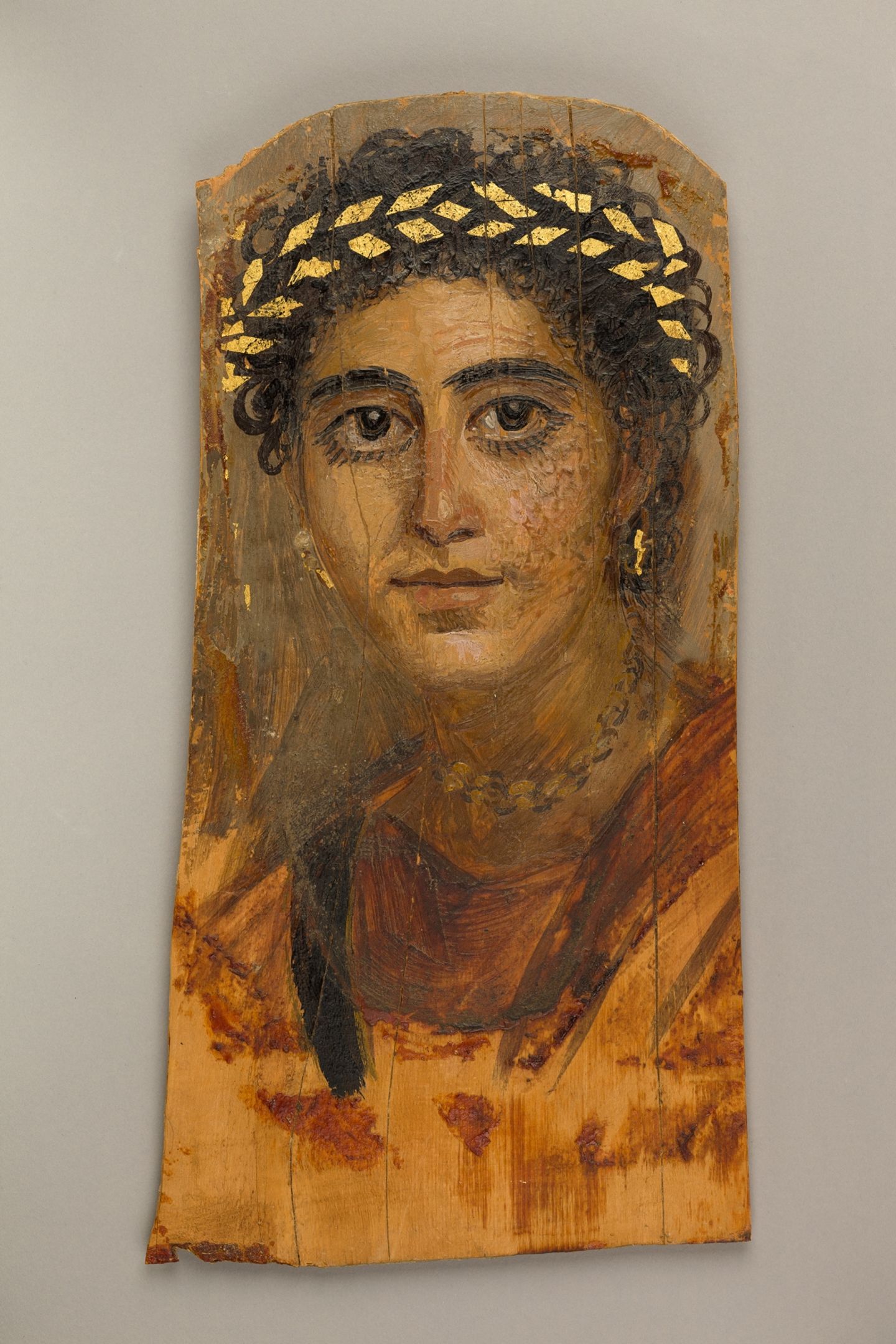 Eine junge Frau mit goldenem Haarkranz und großen Augen mit schlangenförmigen, goldenen Ohrringen