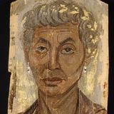 Eine ältere Frau mit grauen Locken und rötlicher Tunika