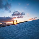 Zwei Leute wandern in der Abenddämmerung ein Gebirge hoch.