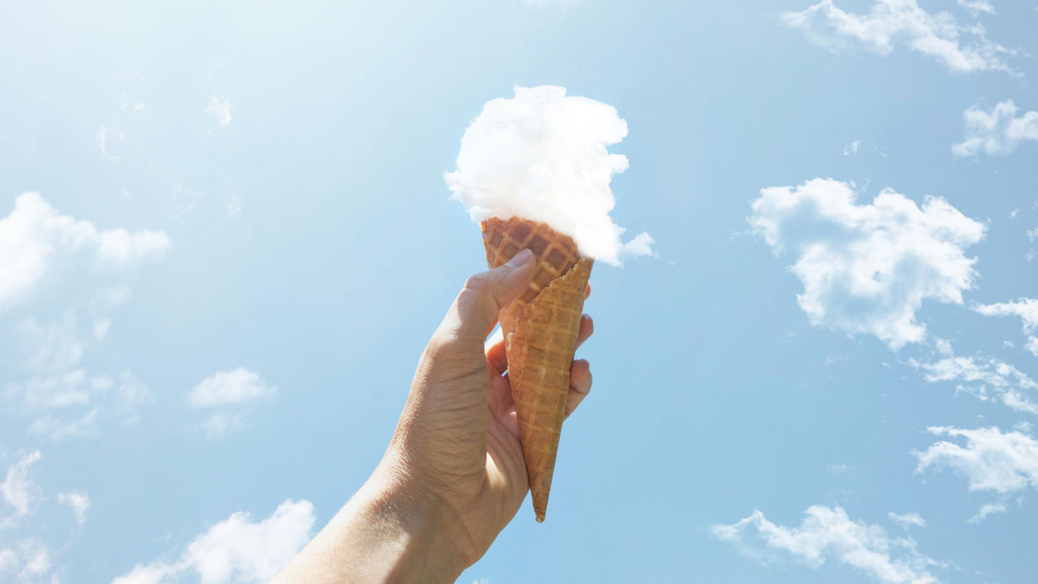 eine Hand hält eine Eiswaffel mit einer Kugel aus einer Wolke in die Luft