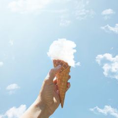 eine Hand hält eine Eiswaffel mit einer Kugel aus einer Wolke in die Luft