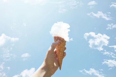 eine Hand hält eine Eiswaffel mit einer Kugel aus einer Wolke in die Luft