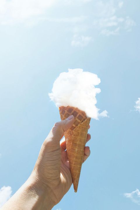 eine Hand hält eine Eiswaffel mit einer Kugel aus einer Wolke in die Luft