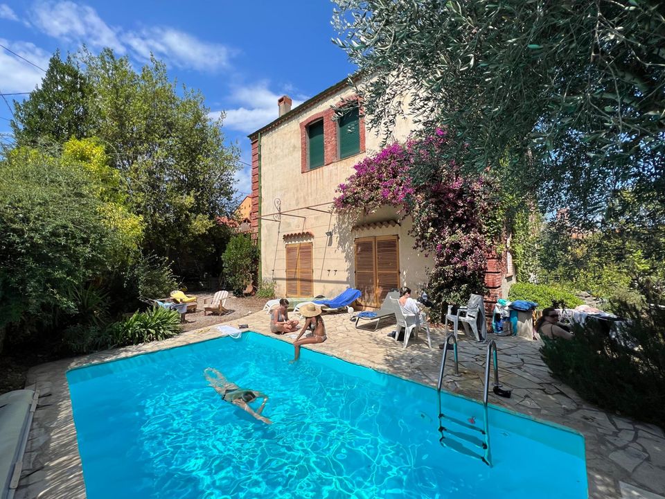 Sommerstimmung am Pool vor dem alten Haus. Einer scwhimmt, der Rest liegt in der Sonne und liest und döst.