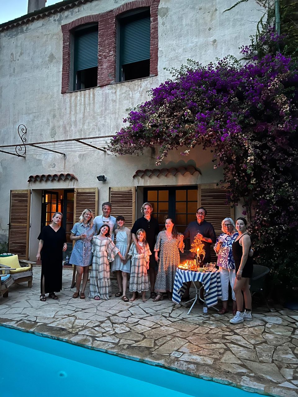 Großfamilie positiert fürs Foto vor dem Haus am Rand des Pools neben einem Tisch. Auf diesem stehen Kerzen. Abendstimmung.
