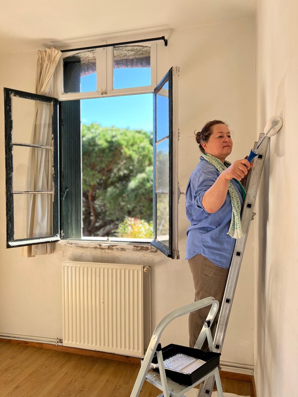 Junge Frau steht auf Leiter und streicht eine Wand.