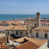 Häuser mit Ziegeldächern und einem Turm vor dem Meer.