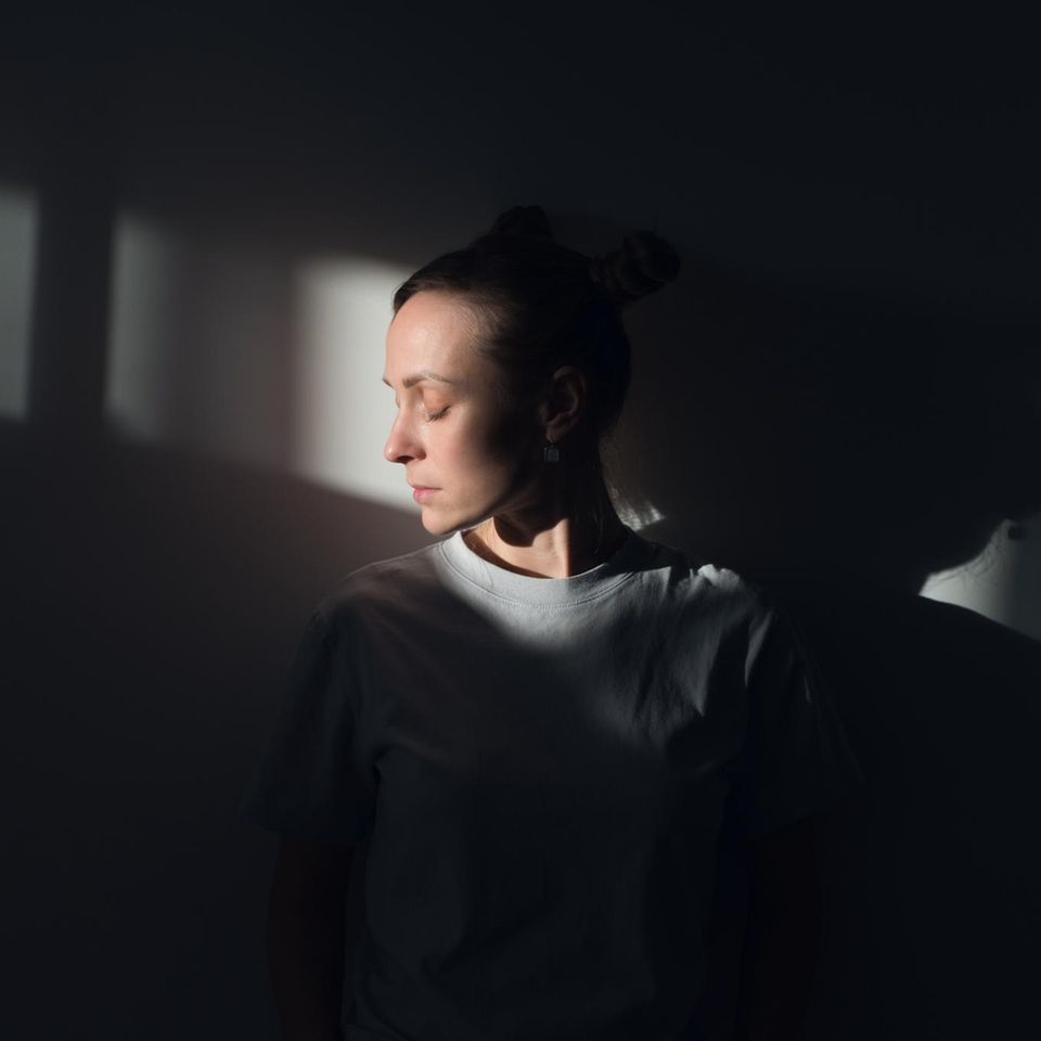 Frau steht im Lichtkegel eines dunklen Zimmers