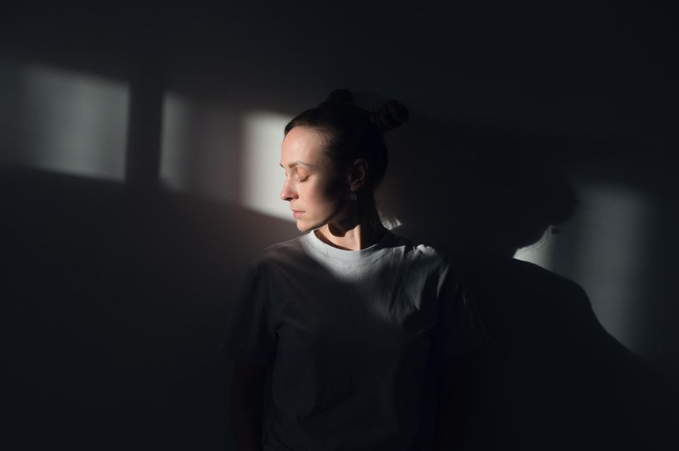 Frau steht im Lichtkegel eines dunklen Zimmers 1.5004
