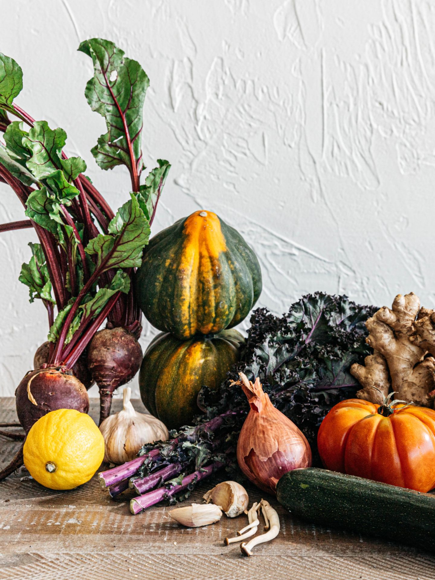 Fotografie: Verschiedene Obst und Gemüsesorten auf einem Holztisch vor einer weißen Wand