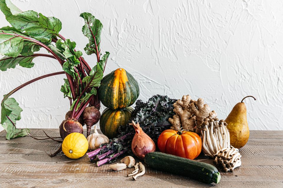 Fotografie: Verschiedene Obst und Gemüsesorten auf einem Holztisch vor einer weißen Wand