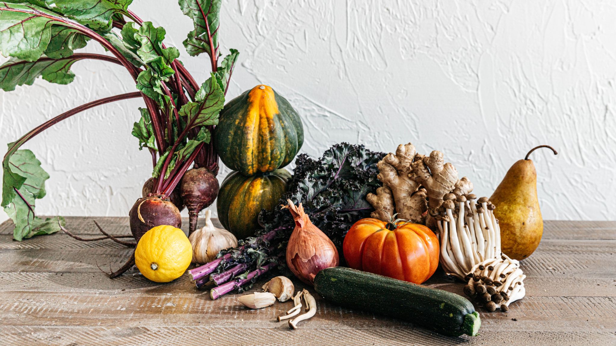 Fotografie: Verschiedene Obst und Gemüsesorten auf einem Holztisch vor einer weißen Wand