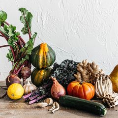 Fotografie: Verschiedene Obst und Gemüsesorten auf einem Holztisch vor einer weißen Wand