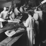 Männer zerteilen an einer langen Tischtafel Fleisch