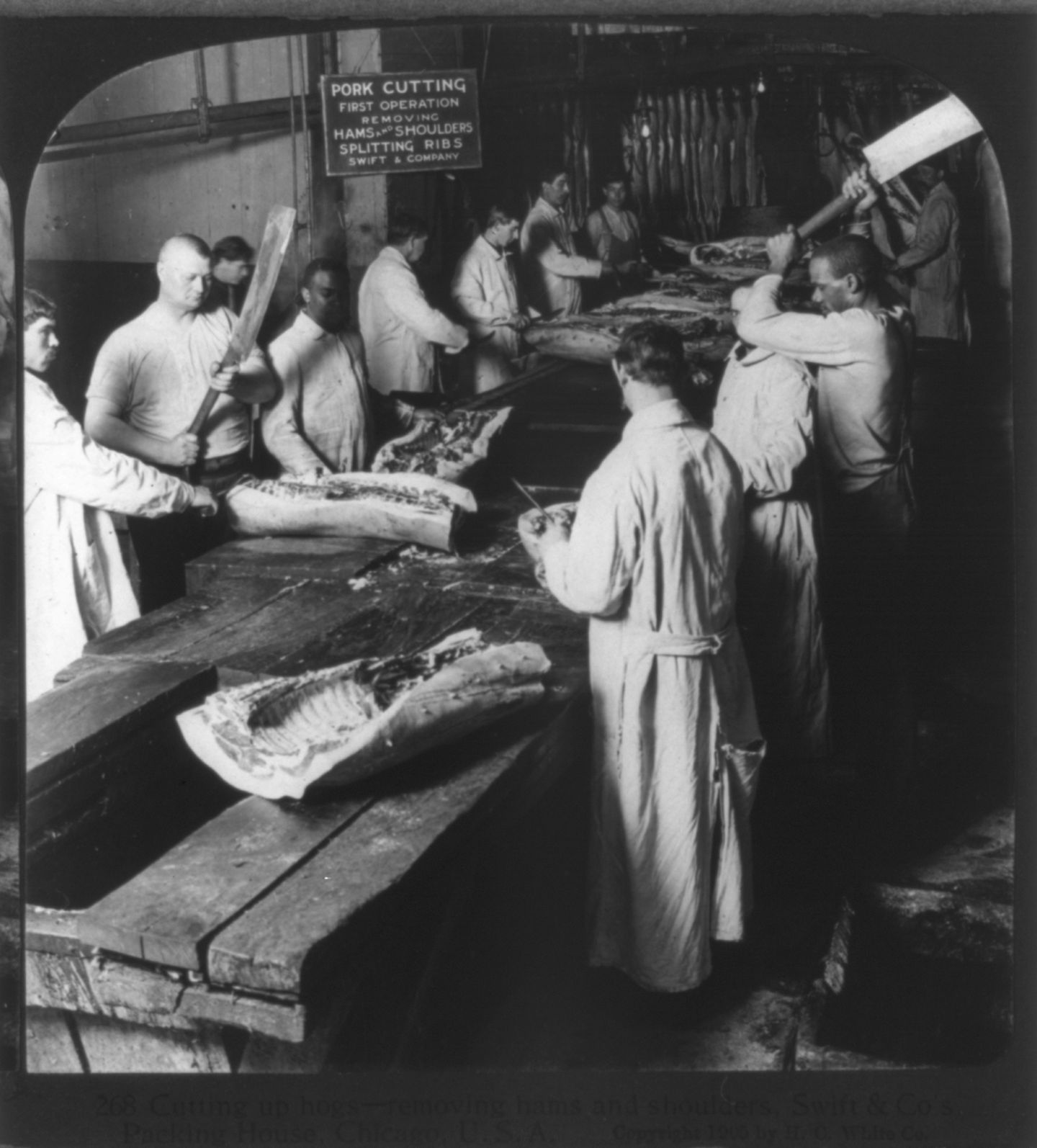 Männer zerteilen an einer langen Tischtafel Fleisch
