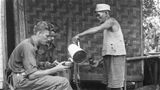 Ein Mann giesst zwei Soldaten Kaffee ein