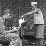 Ein Mann giesst zwei Soldaten Kaffee ein