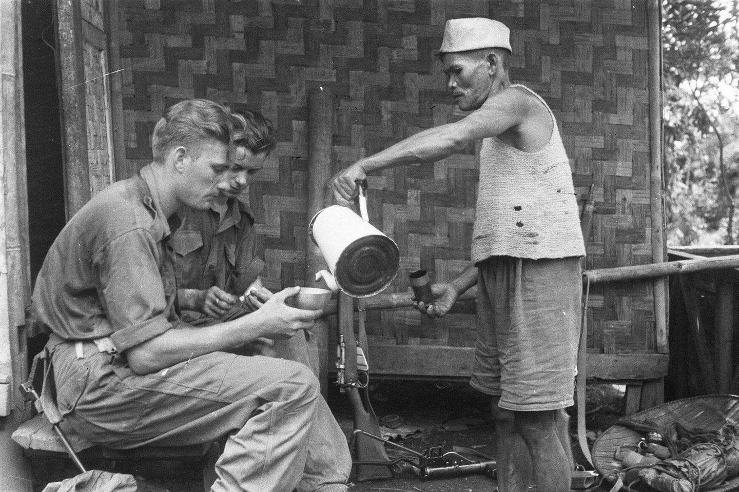 Ein Mann giesst zwei Soldaten Kaffee ein