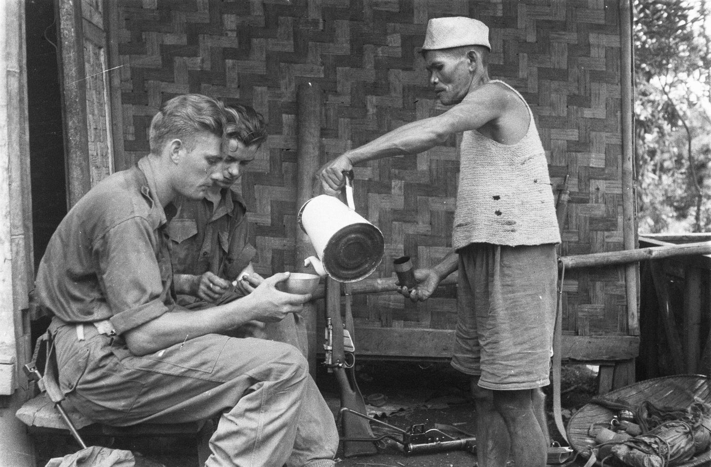 Ein Mann giesst zwei Soldaten Kaffee ein