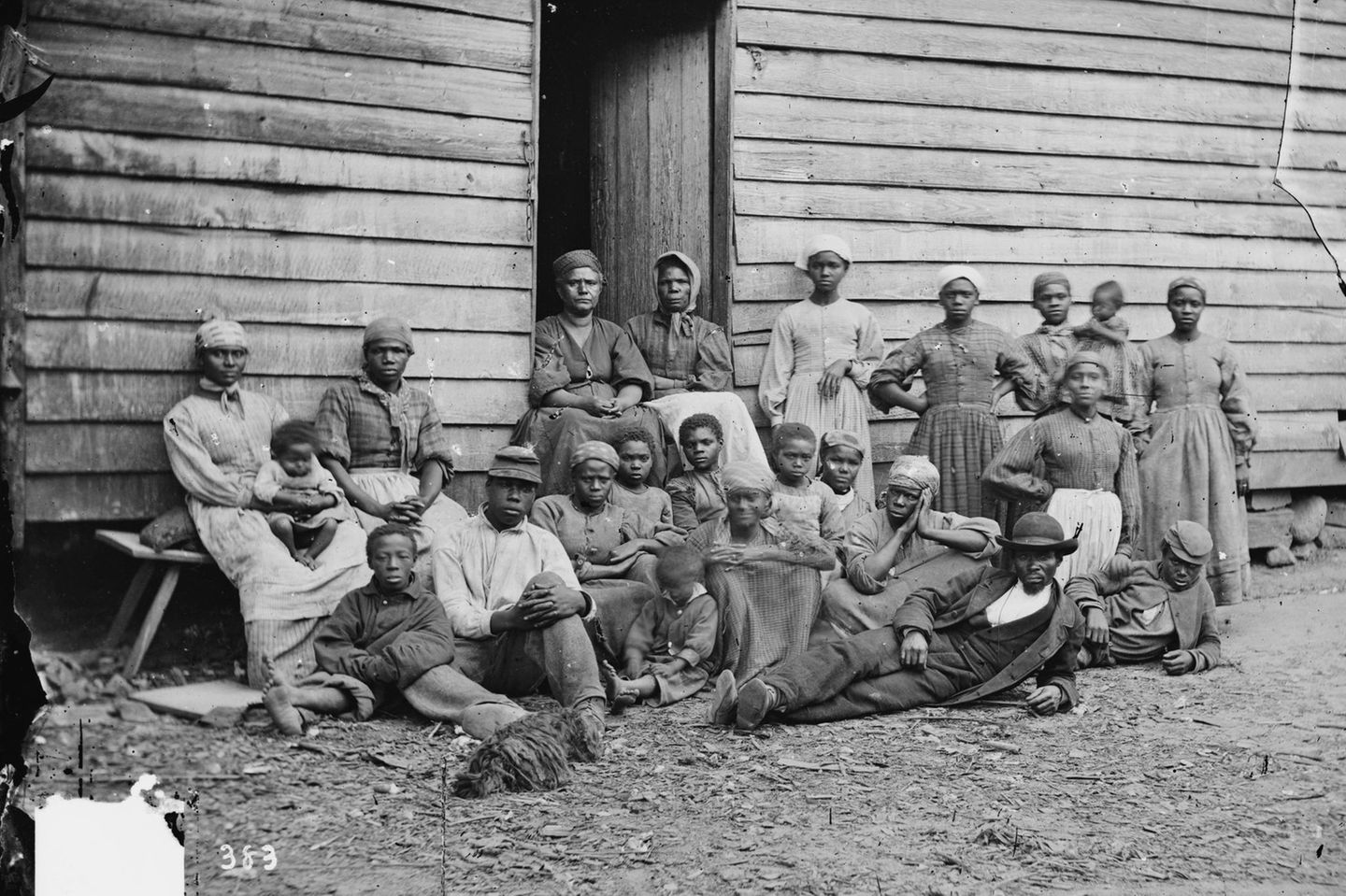 Eine Gruppe von Personen steht und sitzt vor einem Holzhaus