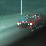 Ein Auto fährt durch die Nacht, während auf der Motorhaube eine Person liegt