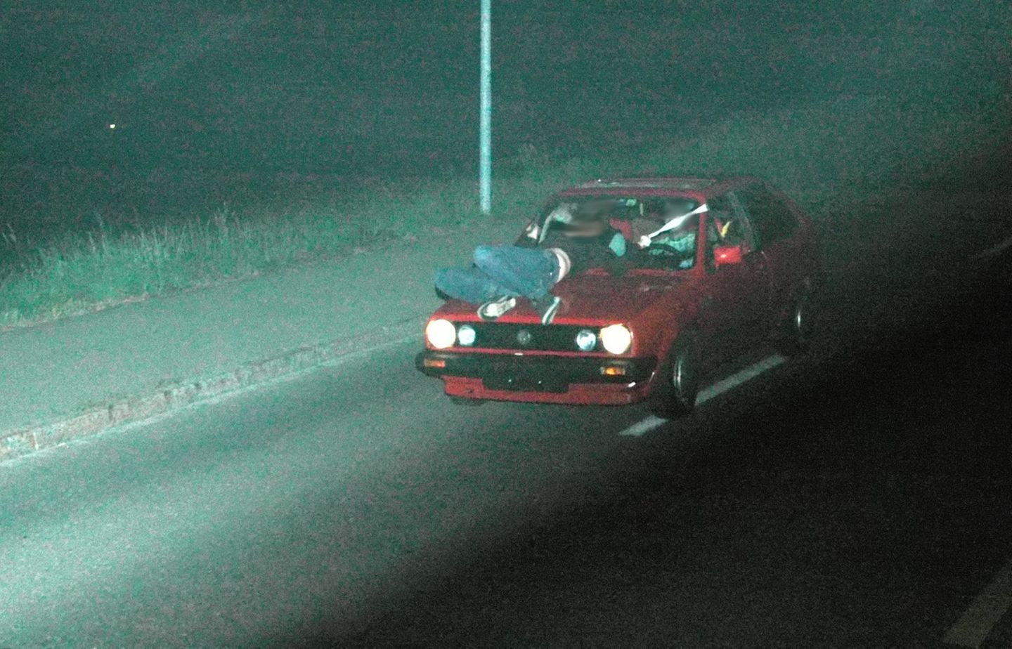 Ein Auto fährt durch die Nacht, während auf der Motorhaube eine Person liegt