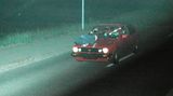 Ein Auto fährt durch die Nacht, während auf der Motorhaube eine Person liegt
