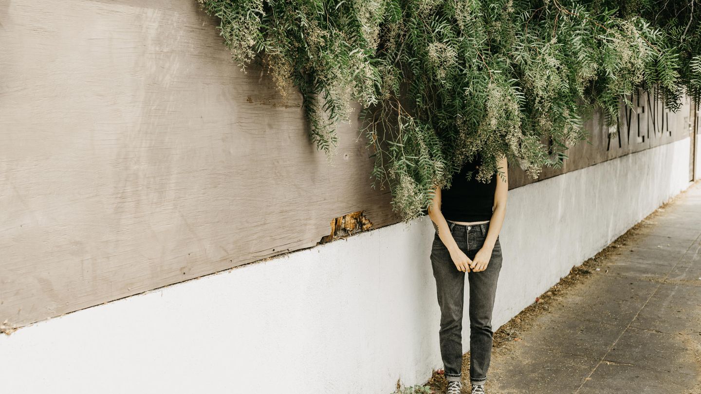 Eine Frau verbirg ihrt Gesicht hinter herabhängenden Zweigen Eine Frau verbirg ihrt Gesicht hinter herabhängenden Zweigen