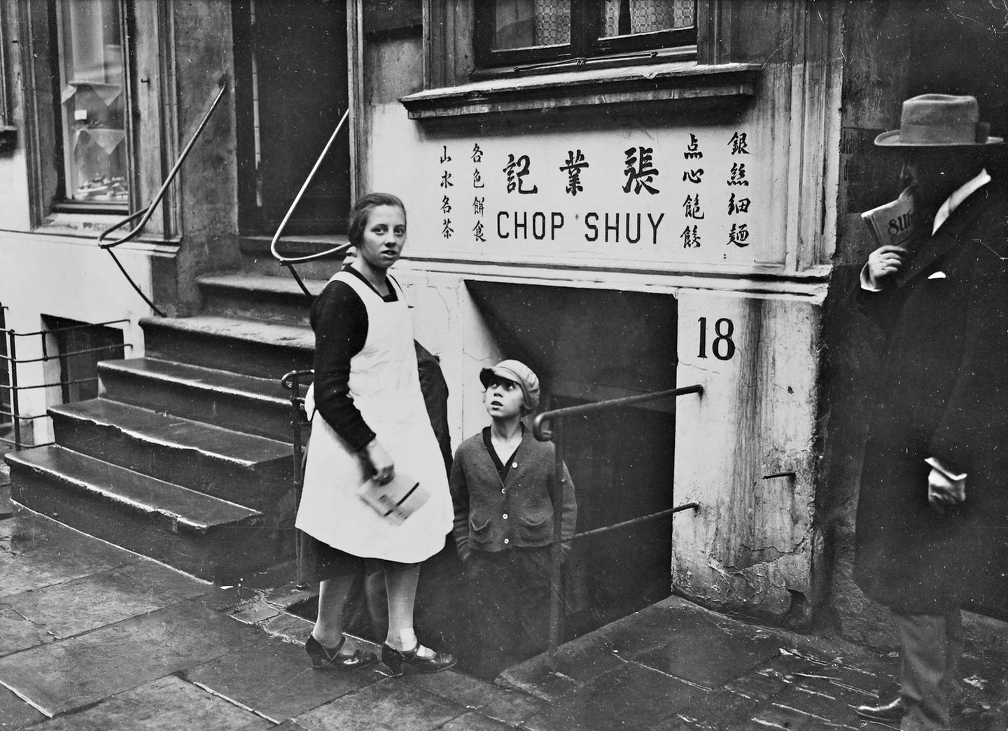 Personen vor einem Kellerlokal, über dessen Eingang "Chop Shuy" und chinesische Schriftzeichen zu lesen sind