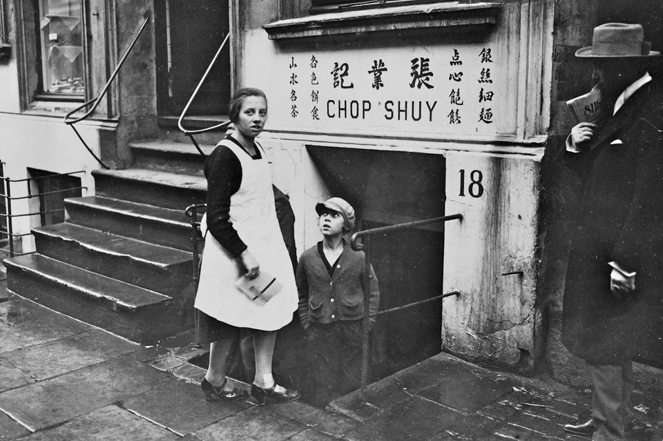 Personen vor einem Kellerlokal, über dessen Eingang "Chop Suey" und chinesische Schriftzeichen zu lesen sind