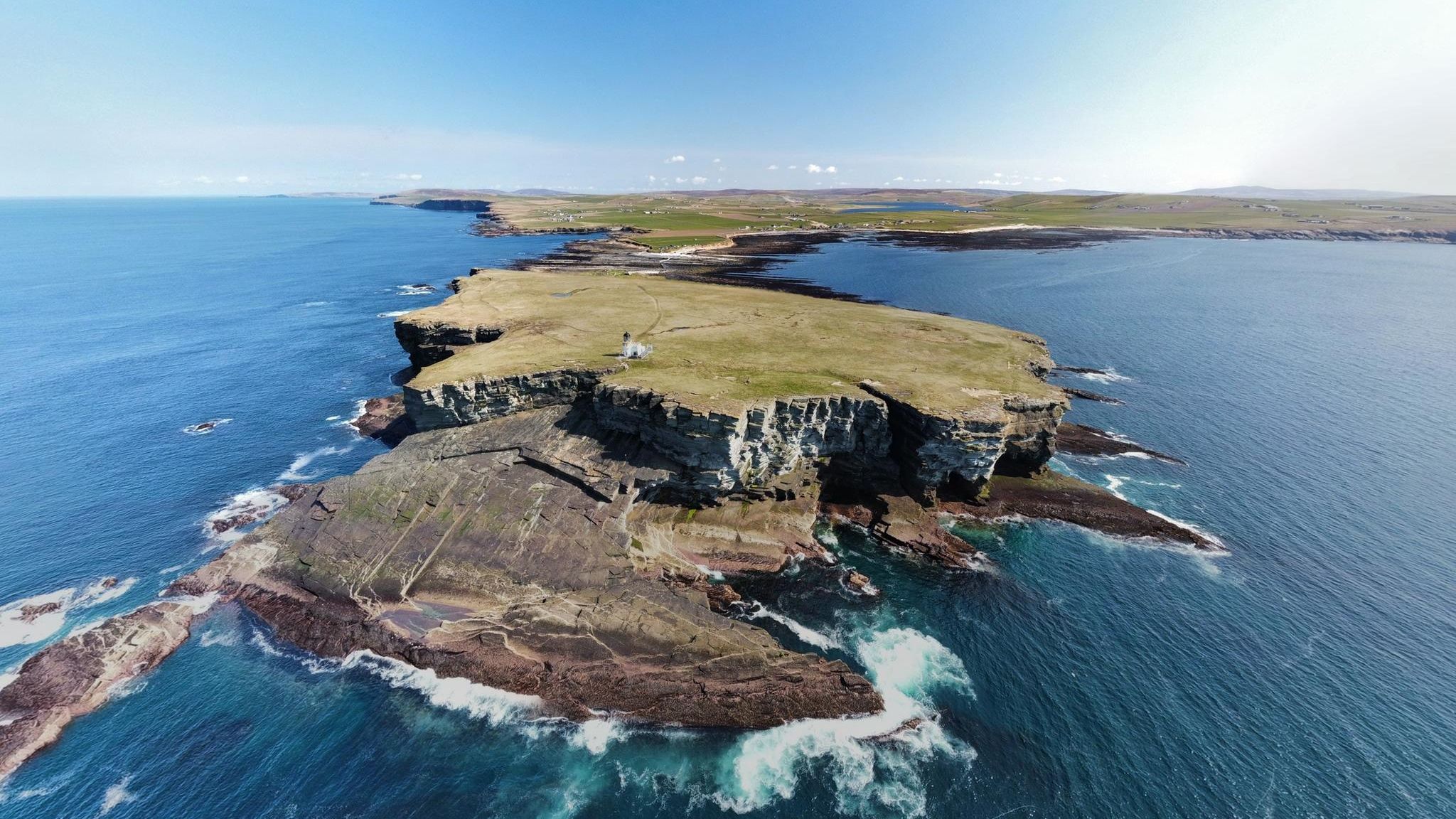 Insel mit flacher Wiese, drumherum steile Klippen. Oben ein kleiner Leuchtturm.