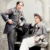 Oskar Wilde im dunklen Anzug, stehend, neben ihm auf einer Bank Alfred Douglas mit Hut und weißen Hosen