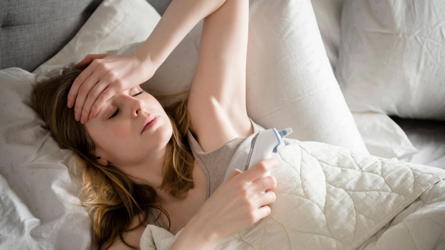 Kranke Frau liegt mit Fieber im Bett und hält sich die Stirn