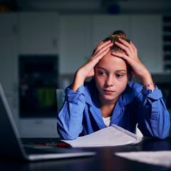 Junge Frau sitzt, mit Kopf in den Händen gestützt, vor dem Laptop
