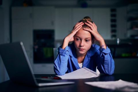 Junge Frau sitzt, mit Kopf in den Händen gestützt, vor dem Laptop