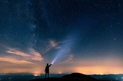 Mann leuchtet mit Taschenlampe ins All – Was ist ein Lichtjahr