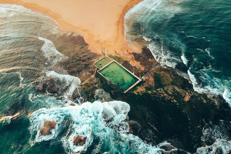 Sandbank, die in Felsen ausläuft, Pools von oben, dahinter das Meer 1.3333