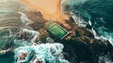 Sandbank, die in Felsen ausläuft, Pools von oben, dahinter das Meer