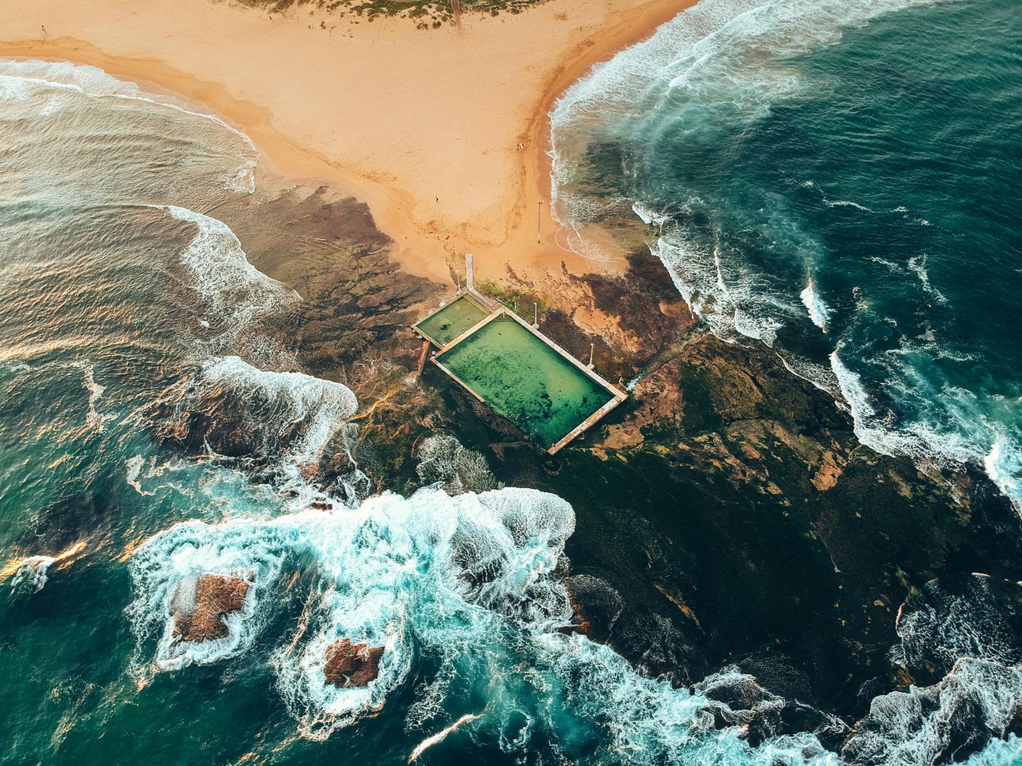 Sandbank, die in Felsen ausläuft, Pools von oben, dahinter das Meer