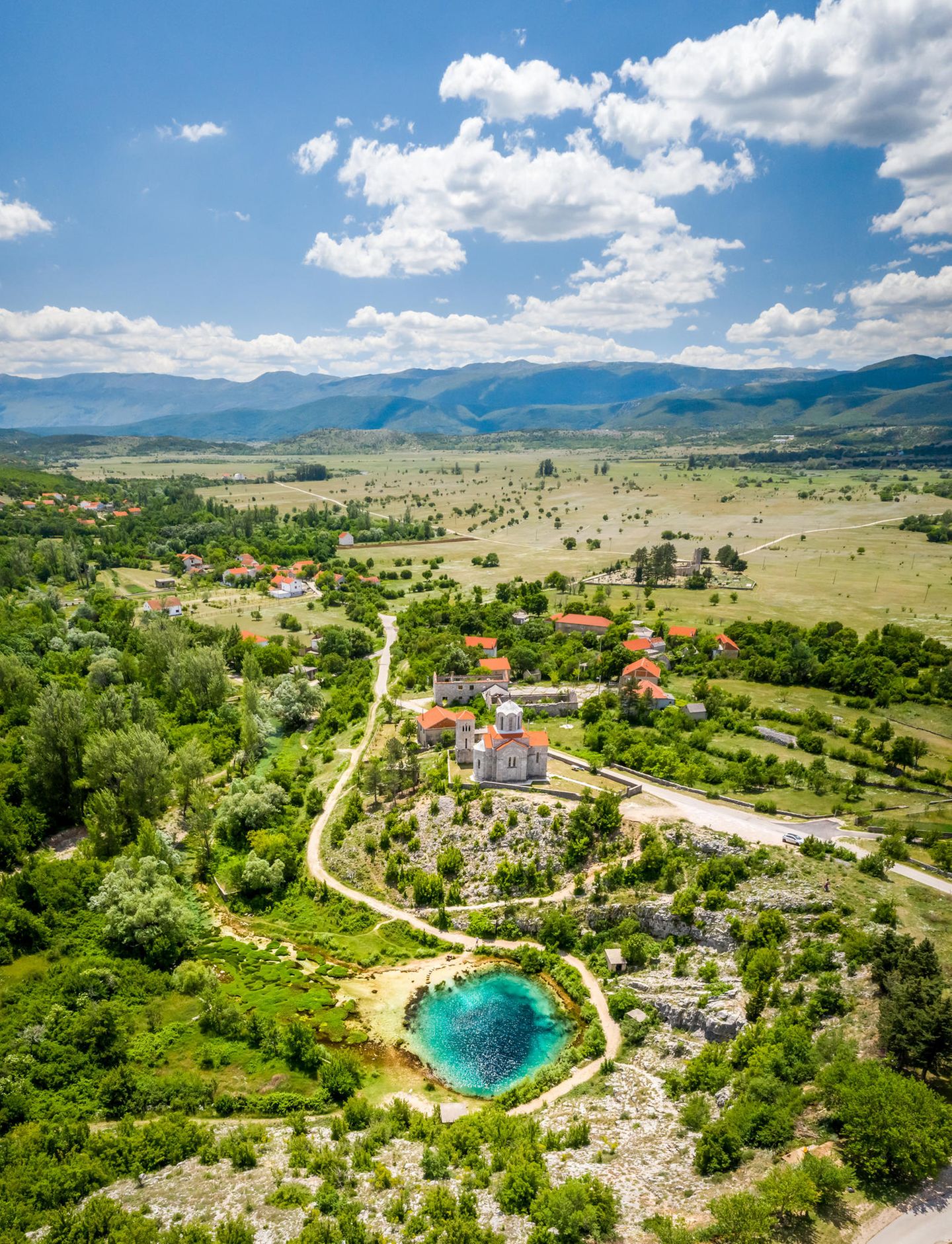 Cetina River Spring, Vrlika, Kroatien Karstlandschaft mit Büschen und Häusern, dazwischen der Quelltopf als kleiner See