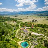 Karstlandschaft mit Büschen und Häusern, dazwischen der Quelltopf als kleiner See