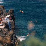 hohe Felsen, unten das Meer, ein Mensch springt rückwärts vom Sprungbrett