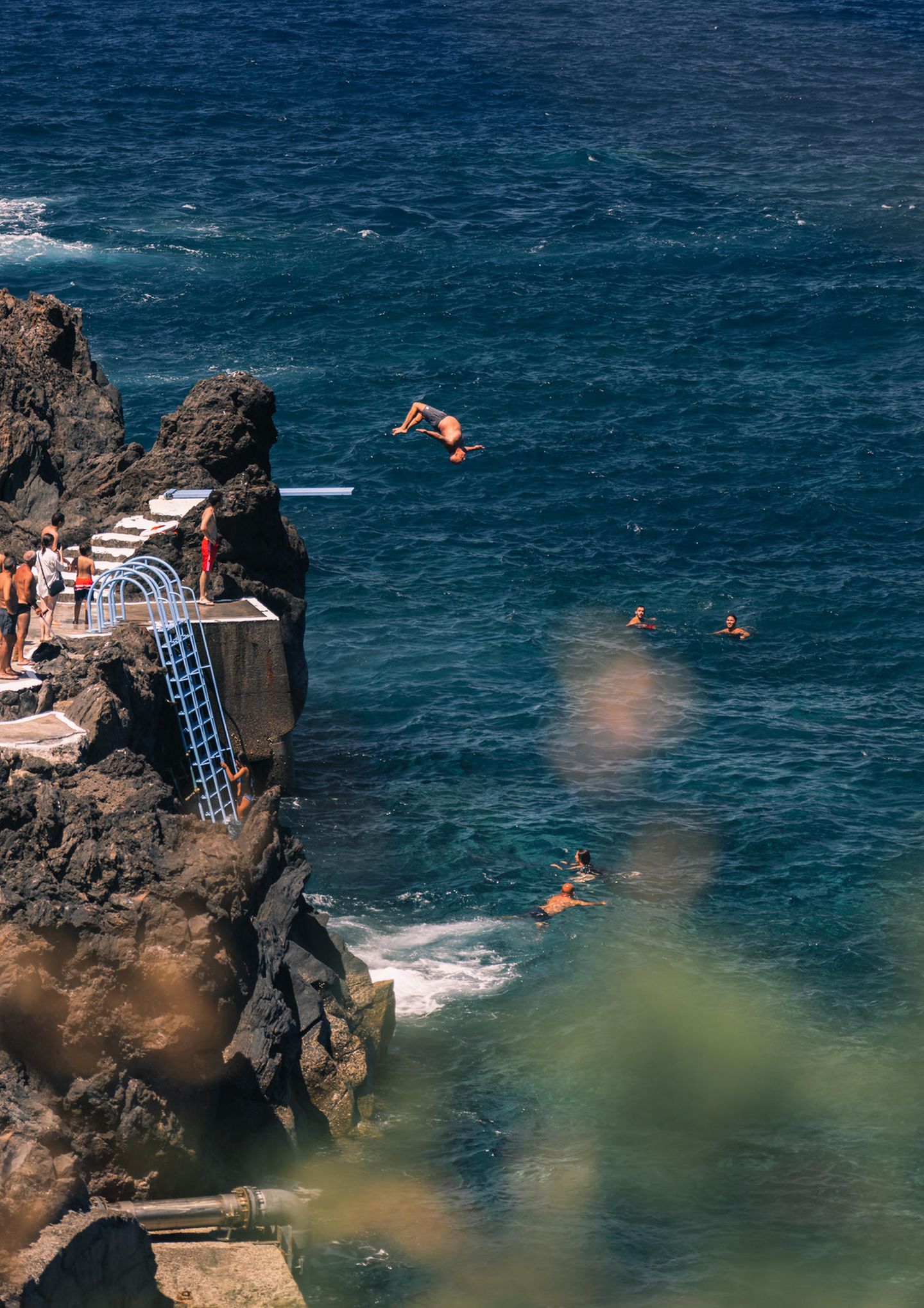 hohe Felsen, unten das Meer, ein Mensch springt rückwärts vom Sprungbrett