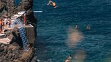 hohe Felsen, unten das Meer, ein Mensch springt rückwärts vom Sprungbrett