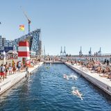 Großes Becken im Hafen, dahinter sieht man Hochhäuser und Kräne