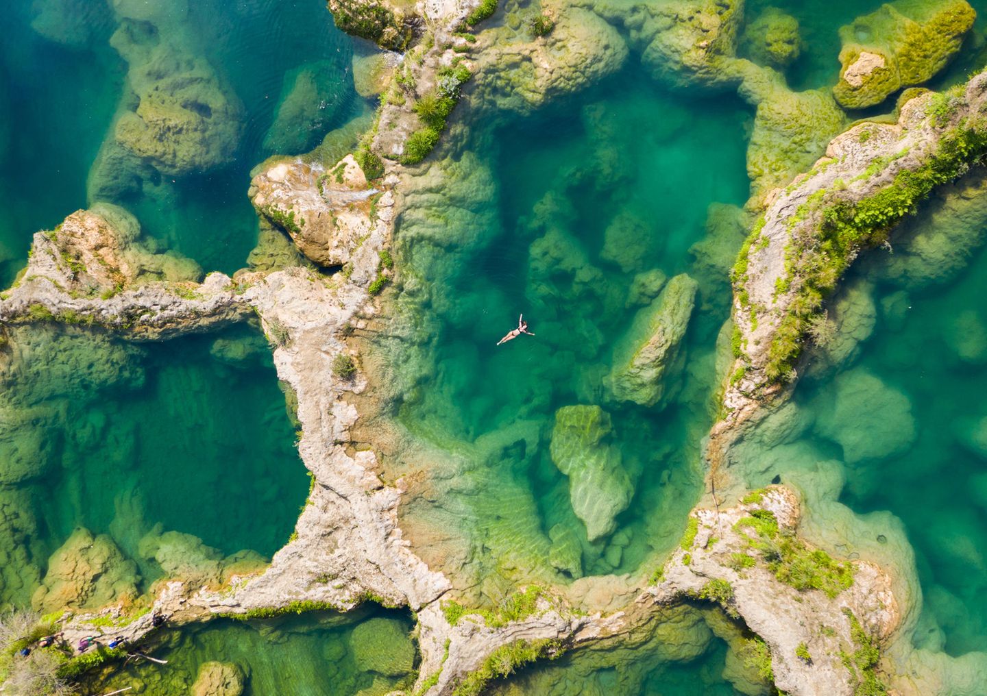 Luftaufnahme von mehreren Becken, von Felsen getrennt. In einem schwimmt eine Frau auf dem Rücken.