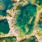 Luftaufnahme von mehreren Becken, von Felsen getrennt. In einem schwimmt eine Frau auf dem Rücken.
