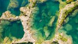 Luftaufnahme von mehreren Becken, von Felsen getrennt. In einem schwimmt eine Frau auf dem Rücken.