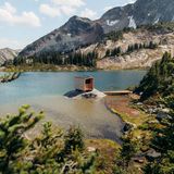 See mit kleinem Felsen, darauf eine modern designte Sauna